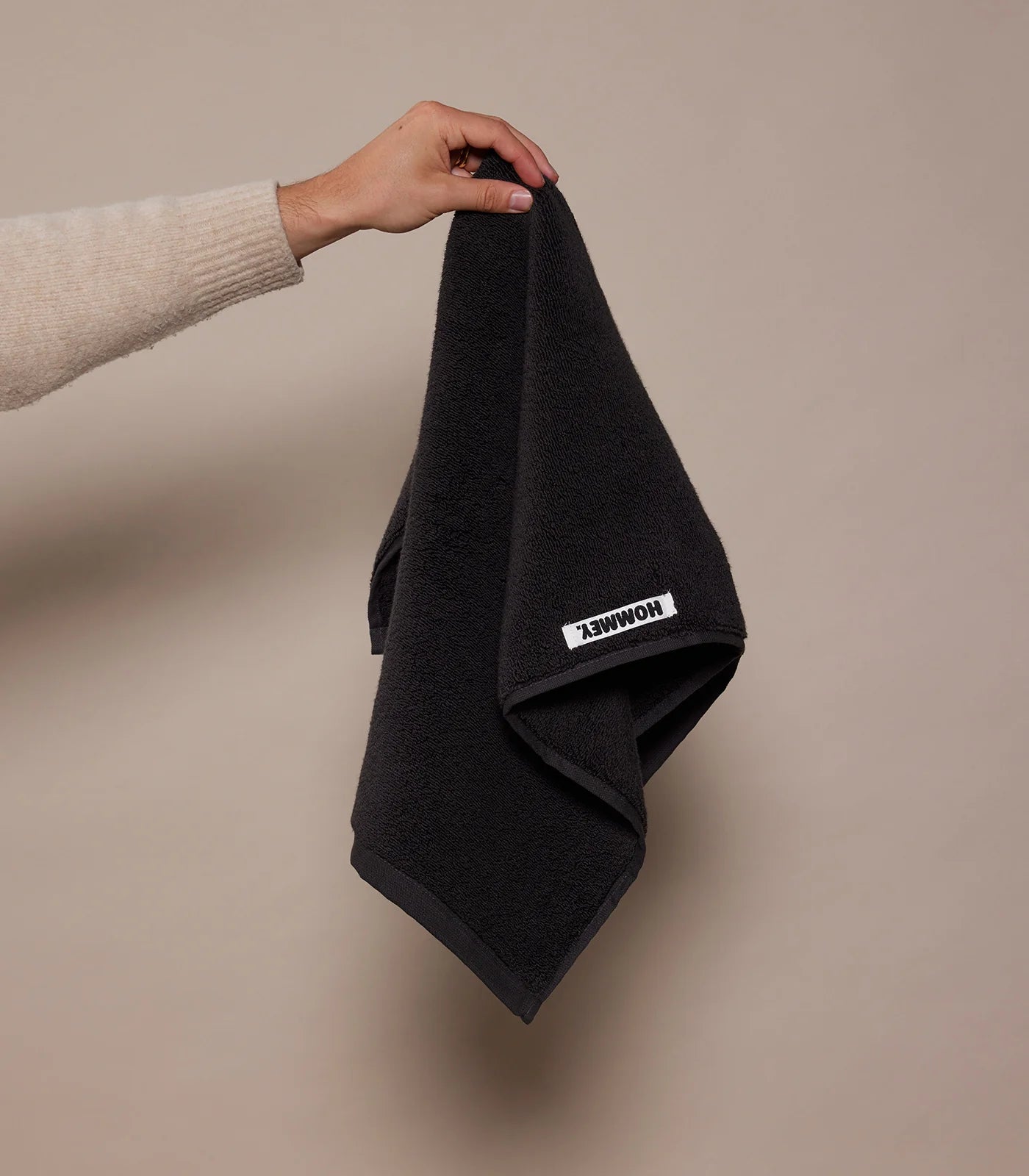 Hand holding a black towel with a brand logo on a beige background