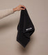 Hand holding a black towel with a brand logo on a beige background