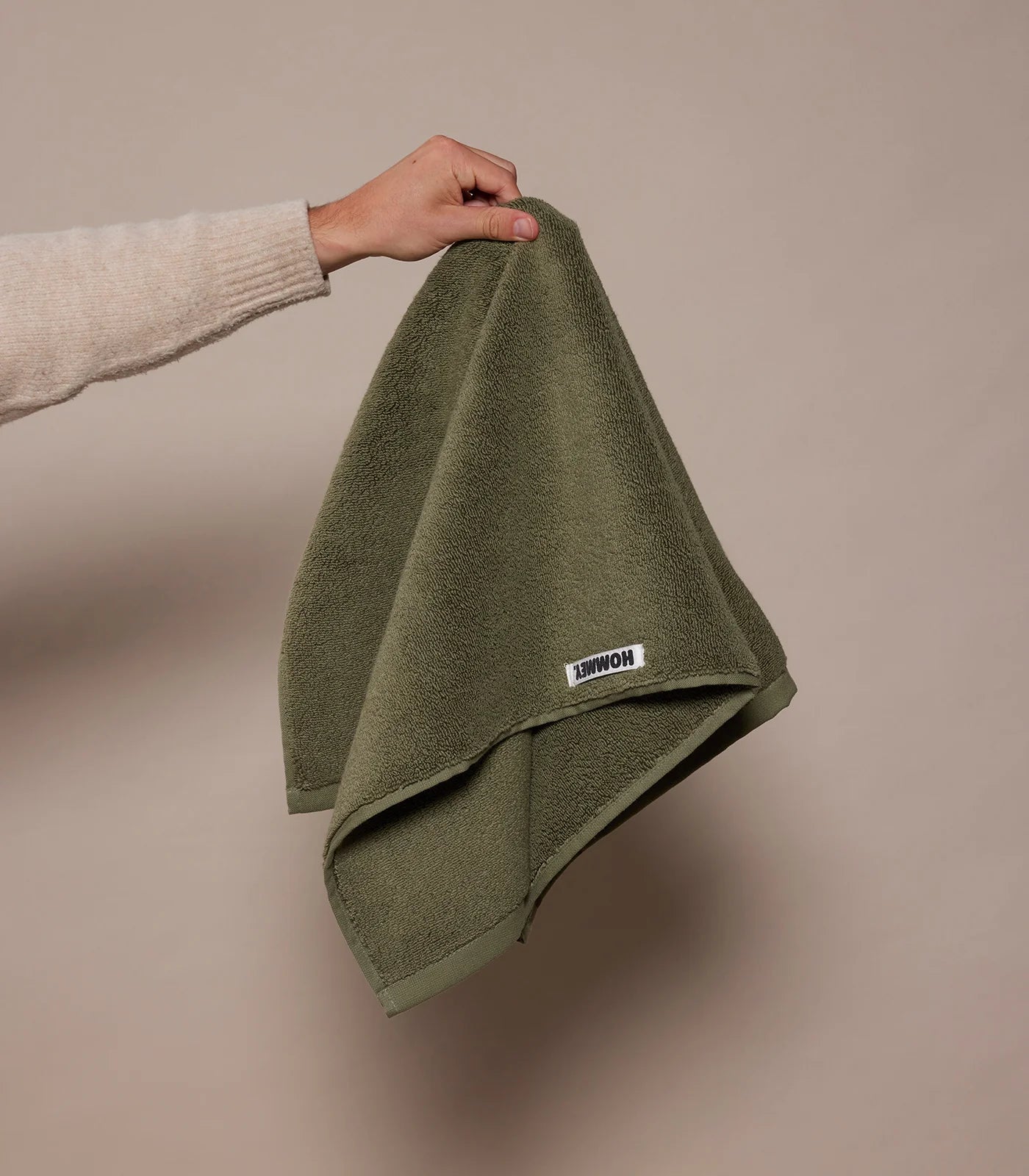 Person holding a green towel with a brand label against a beige background
