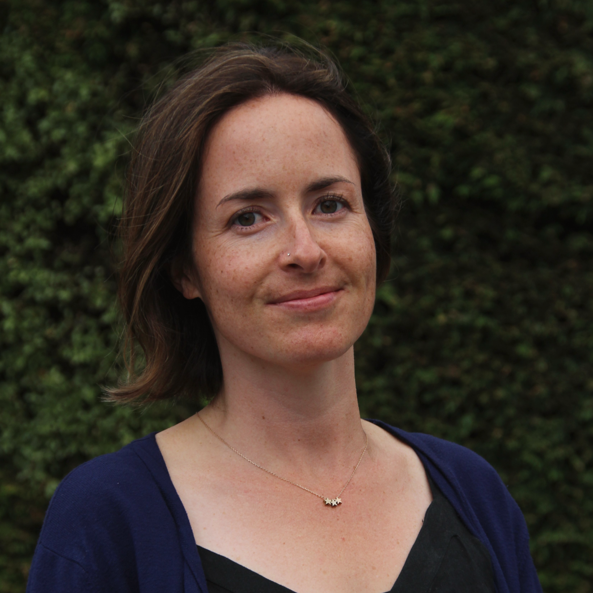Woman standing against a green leafy background