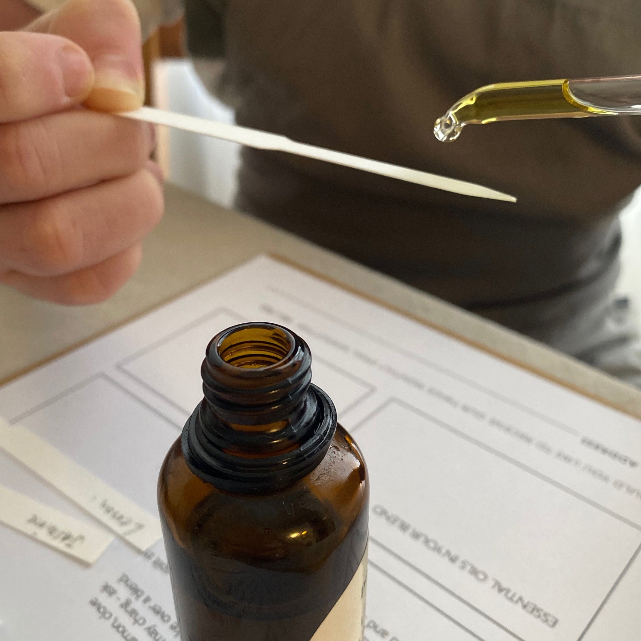Person using a dropper to add essential oils to an amber glass bottle with a blurred background.