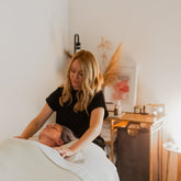 Woman giving a facial to another person in beautifully lit therapy room.