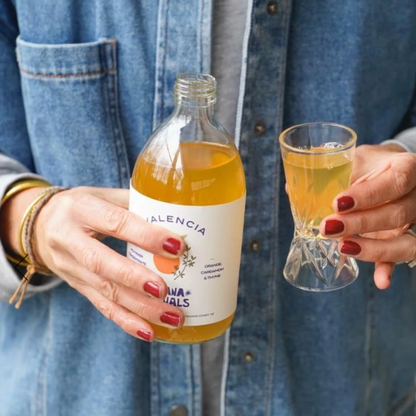Person holding a bottle and a glass of orange infused apple cider vinegar with a &