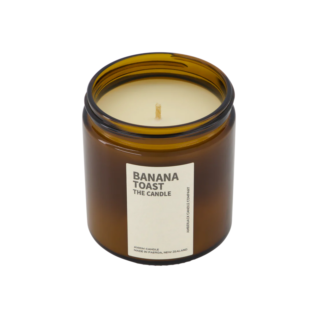 A large amber glass jar with brass lid containing banana toast candle on white background. 