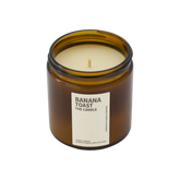 A large amber glass jar with brass lid containing banana toast candle on white background. 