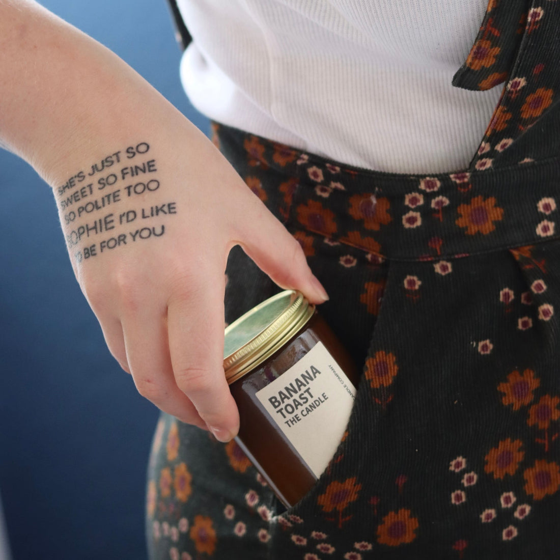 Amber glass jar with brass lid containing banana toast candle being pulled from a pocket of brown floral cord pants.