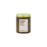 Amber glass jar with brass lid containing brown sugar and fig candle on white background. 