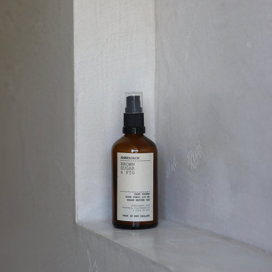An amber glass bottle of Brown Sugar and Fig room spray on a concrete shelf. 
