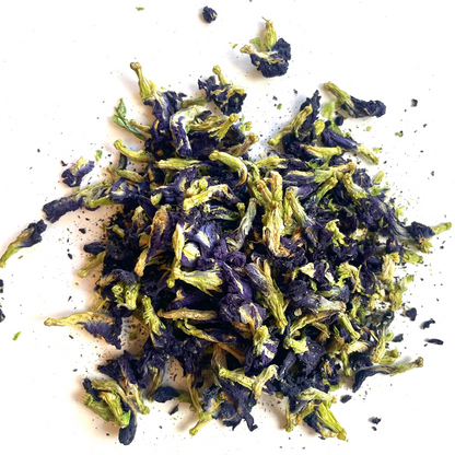 A small pile of dried butterfly pea flowers, showing deep purple-blue petals mixed with bright green stems, scattered on a plain white background.
