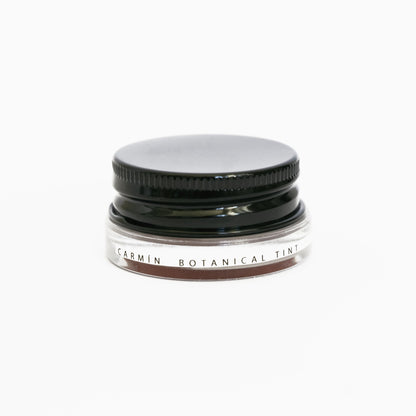 A small glass pottle of Carmín lip tint on white background. 