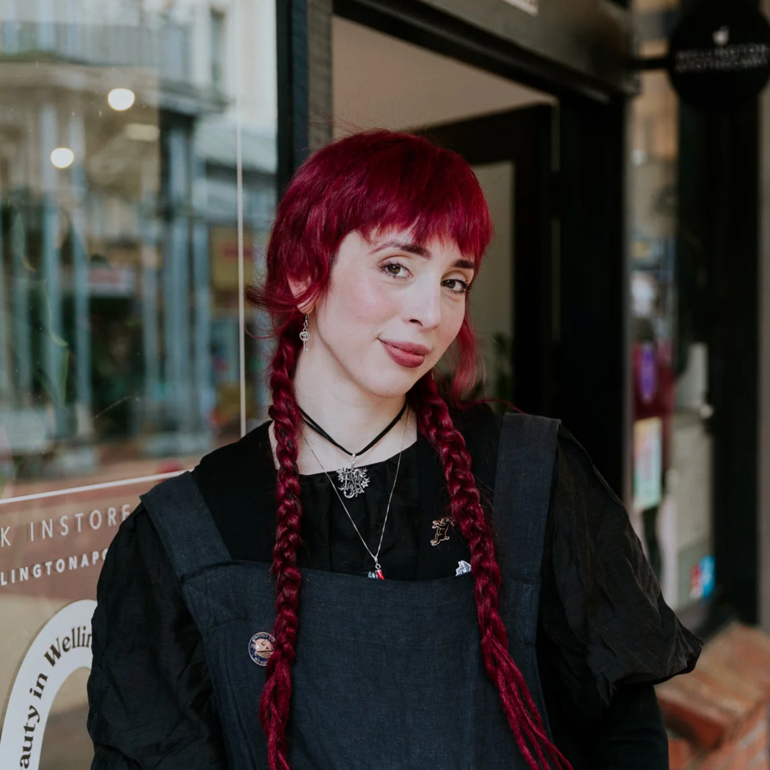 Person with red hair styled in braids wearing a black outfit in an urban setting.