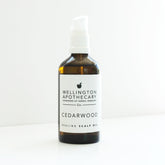 An amber glass bottle with a white pump top filled with Cedarwood Scalp Oil  on a white bench. 