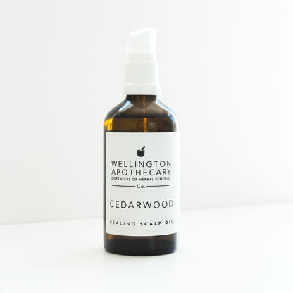 An amber glass bottle with a white pump top filled with Cedarwood Scalp Oil  on a white bench. 