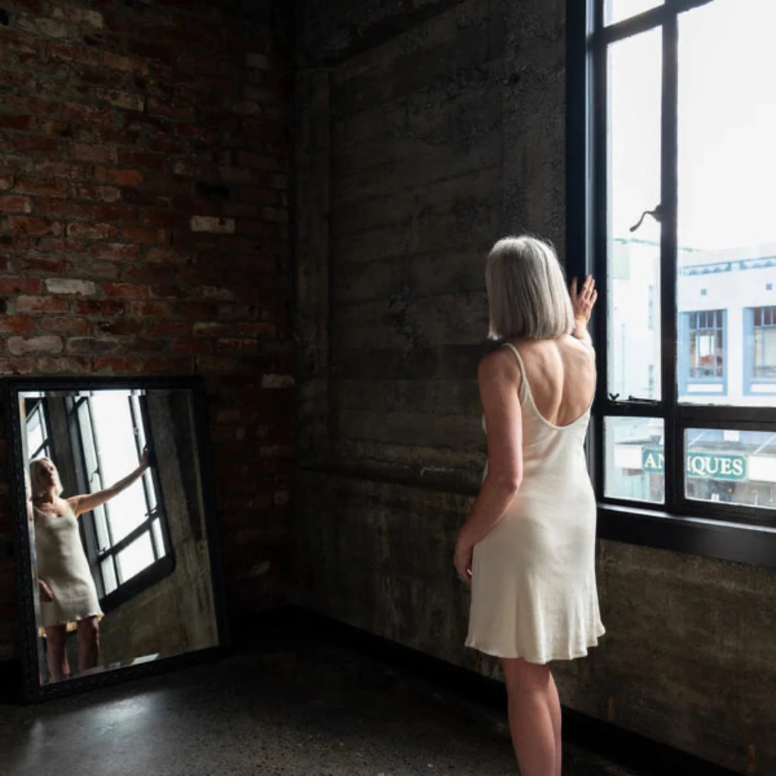 Woman in a white dress standing by a window in an urban setting