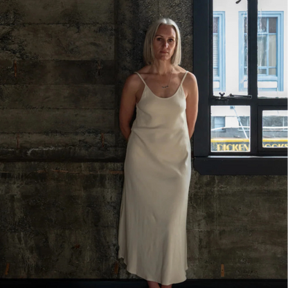 Woman in a white dress standing against a textured wall with a window in the background