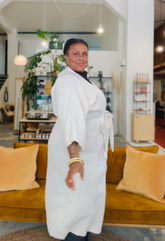 Person wearing a white robe standing in a room with a couch and plants.