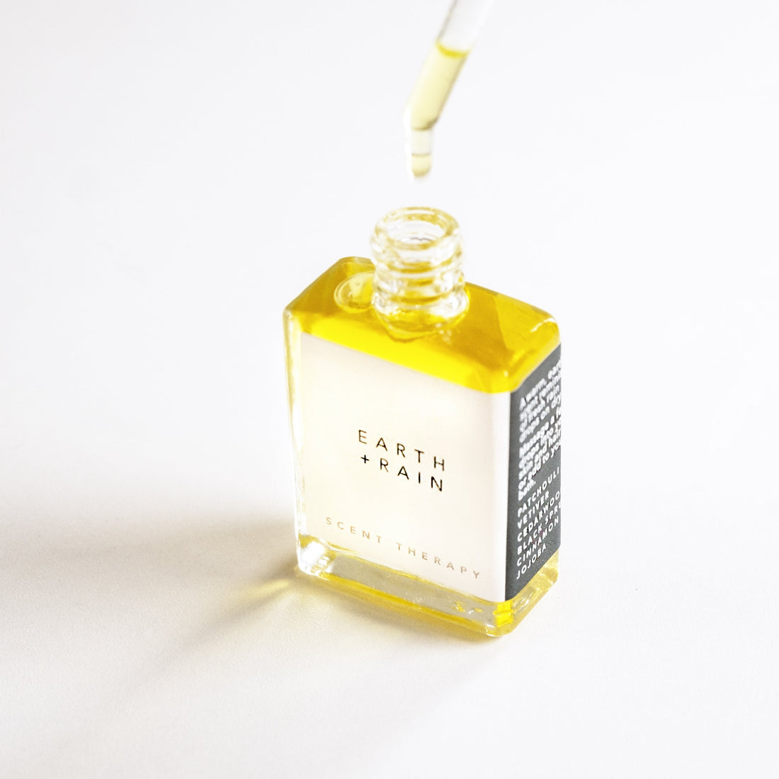 A square glass bottle of the Earth + Rain scent therapy oil blend, with the dropper top dripping. 