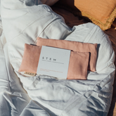 Two petal coloured linen eye pillows on a duvet in the sunshine.