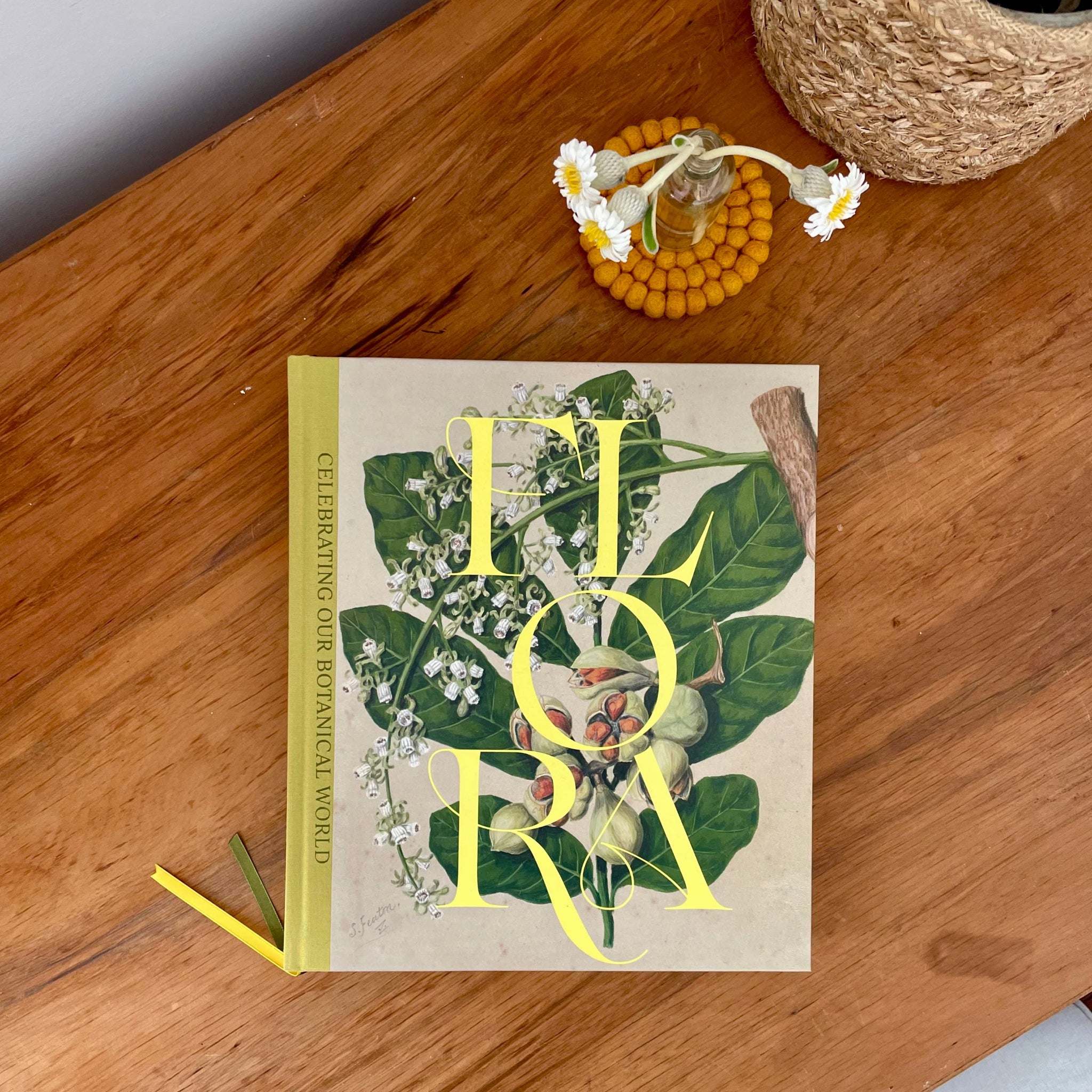 A book called FLORA on a wooden desk with daisies