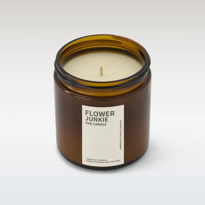 Flower junkie candle in amber glass jar with lid off on white background. 
