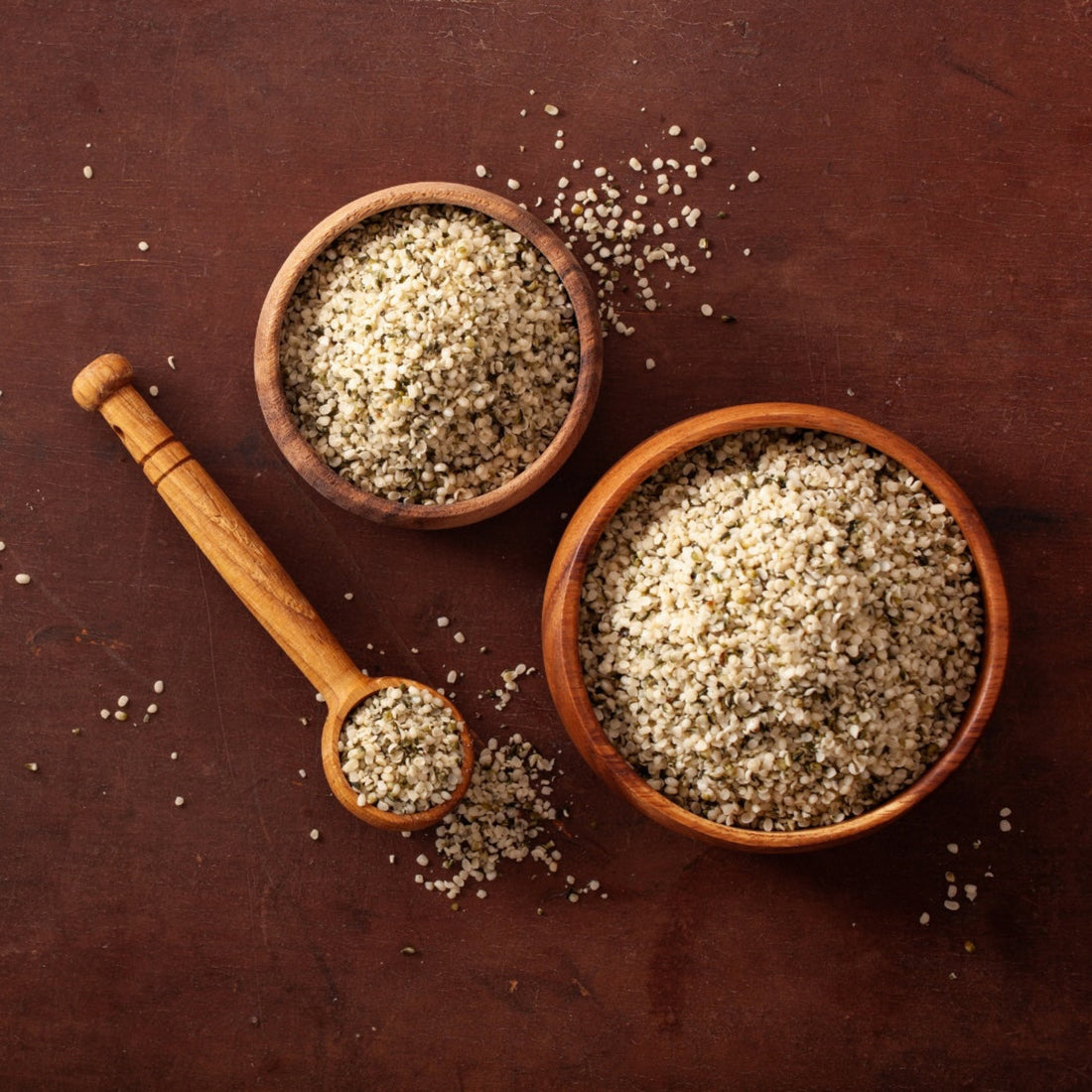 Wooden bowls and wooden spoon holding hempseeds on a brown bench. 