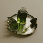 Glass dropper bottle with green liquid on a metal tray against a neutral background