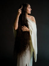 Woman with long hair brushing it, wearing a white garment against a dark background