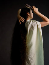 Woman in a light green saree combing her hair against a dark background
