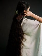 Person brushing their long hair with a wooden comb against a dark background