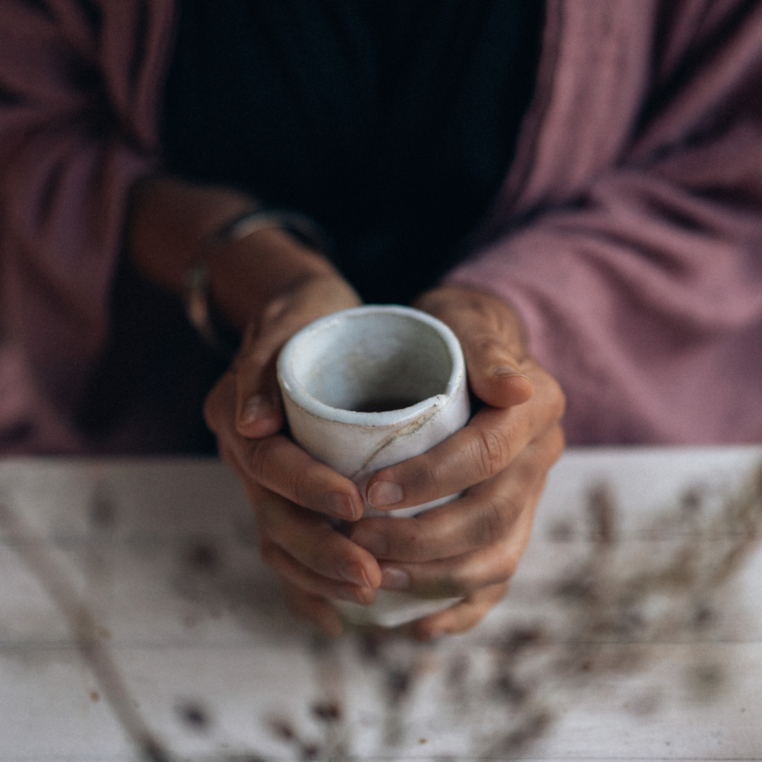 A woman in a lilac cardigan holding an earthy white ceramic cup. 