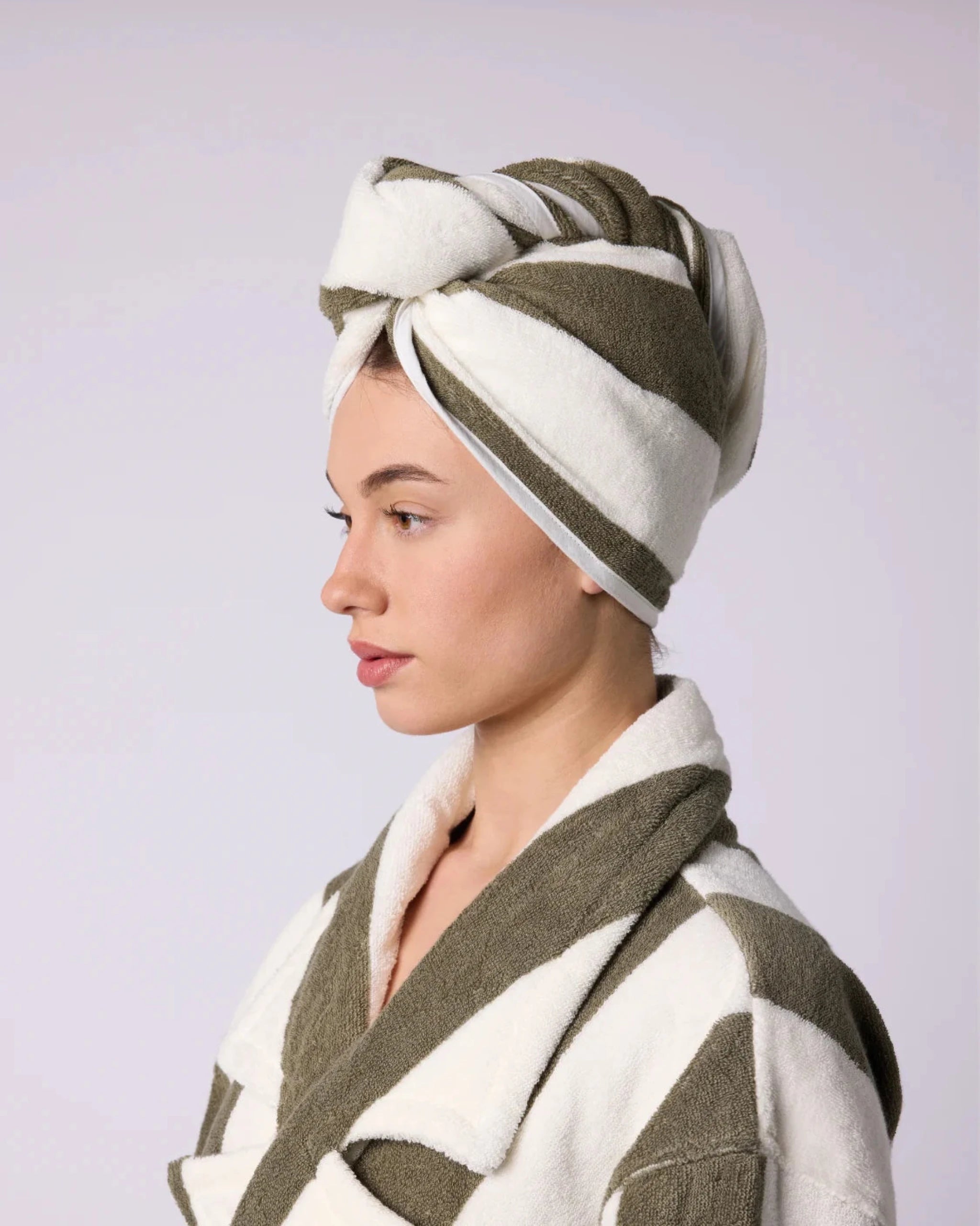 Woman wearing a green and white striped towel hair wrap on her head with a matching robe.