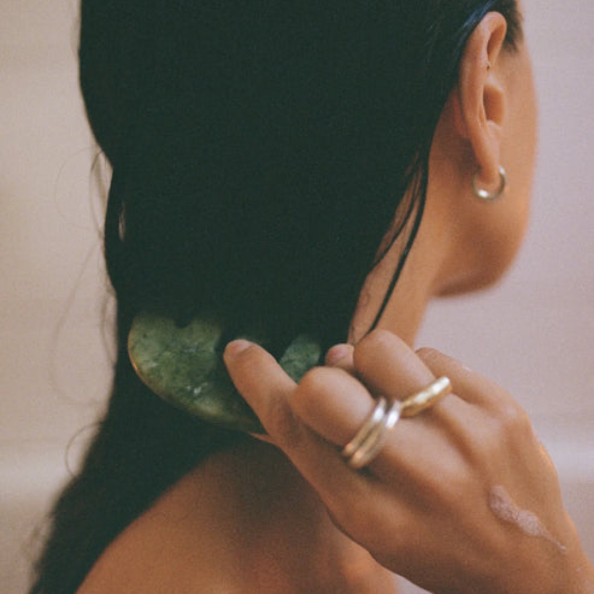 Person with long dark hair using a green jade comb on a neutral background