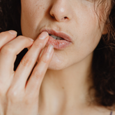 A close up of a woman applying lip balm with her ring finger. 
