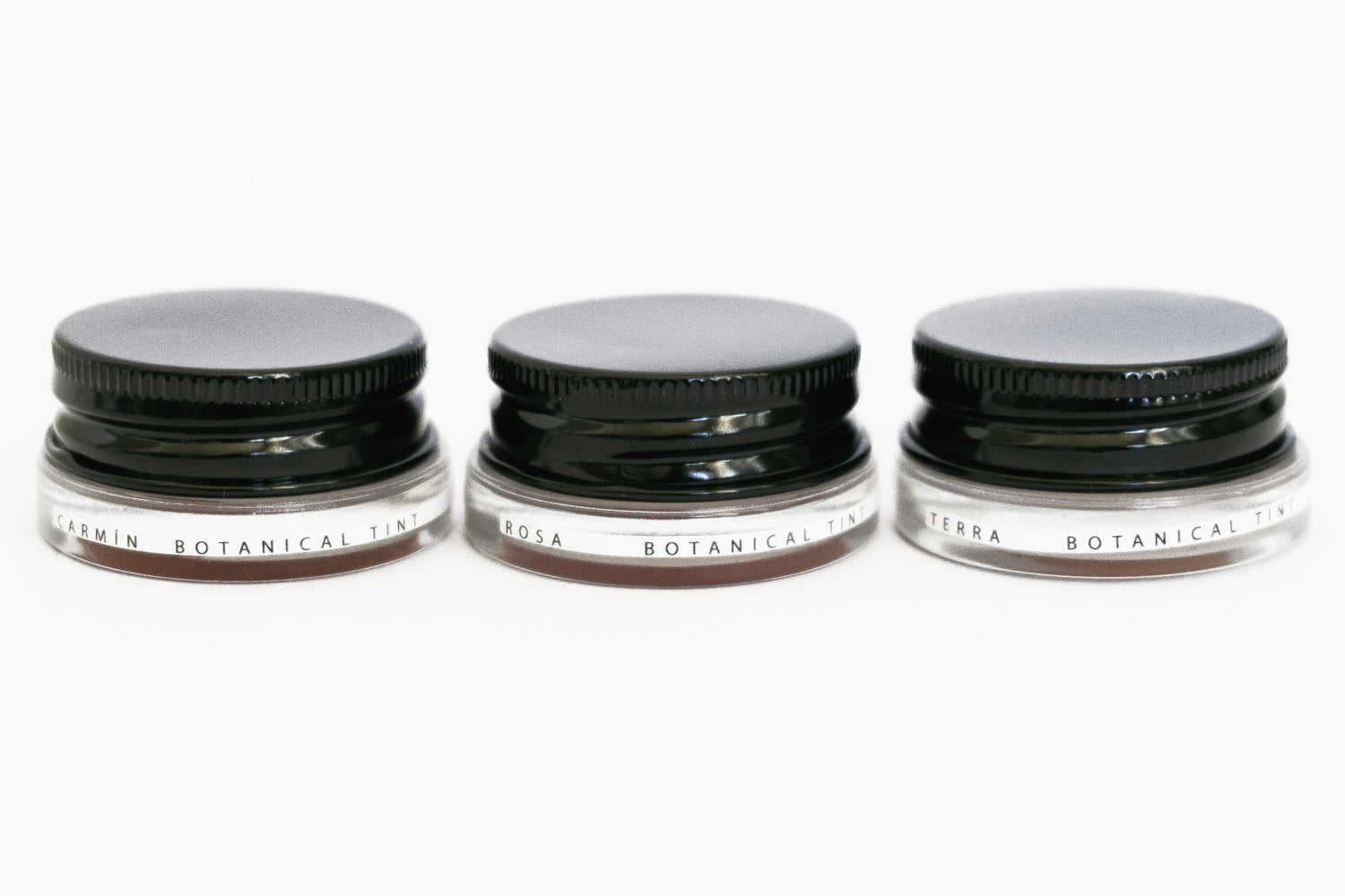 Three glass pottles with black aluminium lids in a row containing three shades of natural pigment lip tints. 