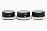 Three glass pottles with black aluminium lids in a row containing three shades of natural pigment lip tints. 