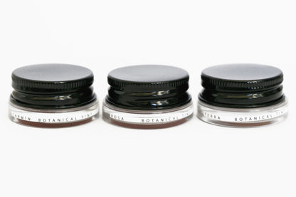 Three glass pottles with black aluminium lids in a row containing three shades of natural pigment lip tints. 