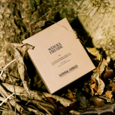 Box of Manuka Fireside candles by National Candles on a natural background with leaves and wood.