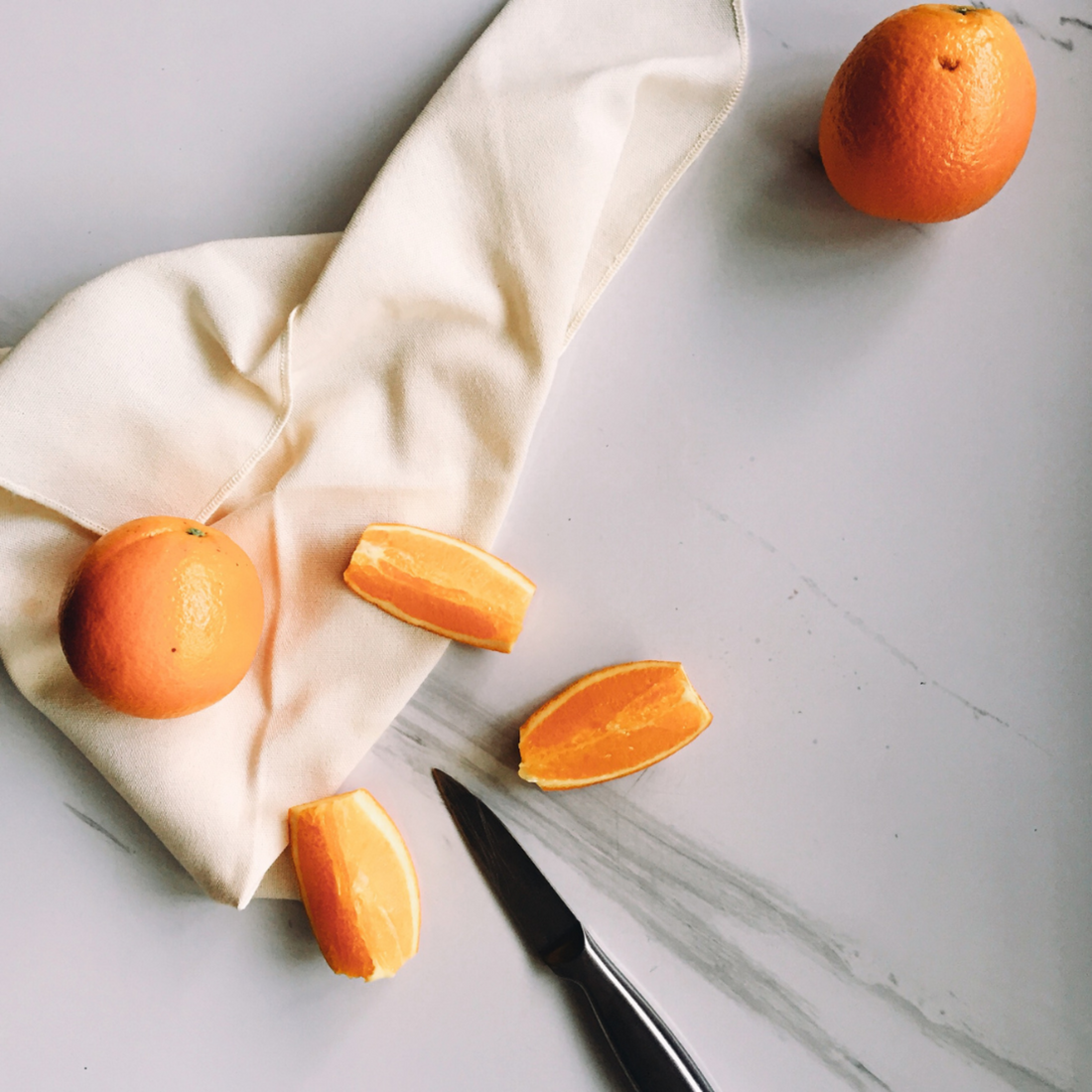 Oranges sliced into wedges on kitchen bench top with cream colour napkin.