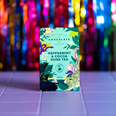 Peppermint cocoa husk tea package with colorful design on a tiled surface with multicoloured lights in the background