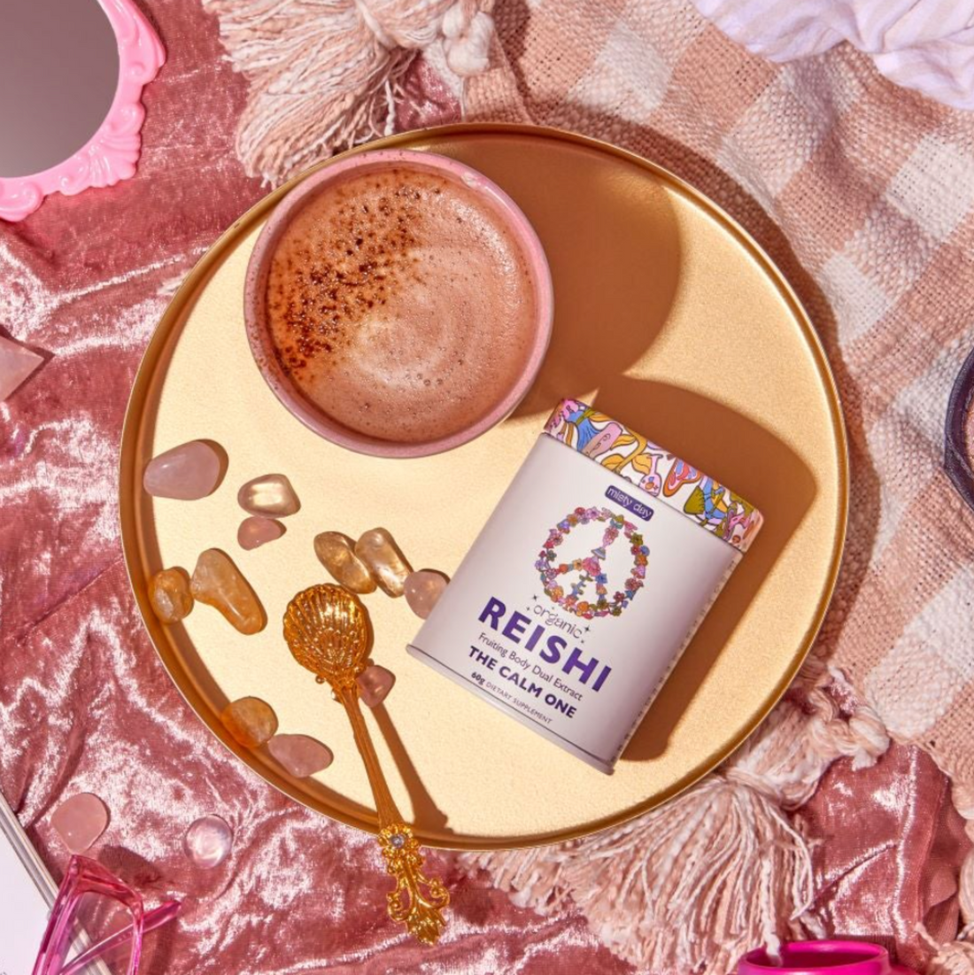 A cup of reishi on a golden tray with rose quarts and others pink paraphernalia.