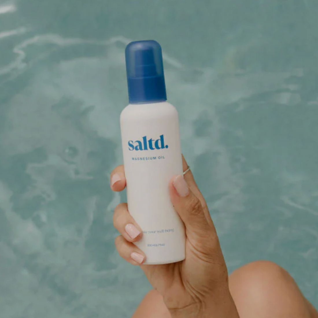 Hand holding a bottle of saltd product against a textured gray background