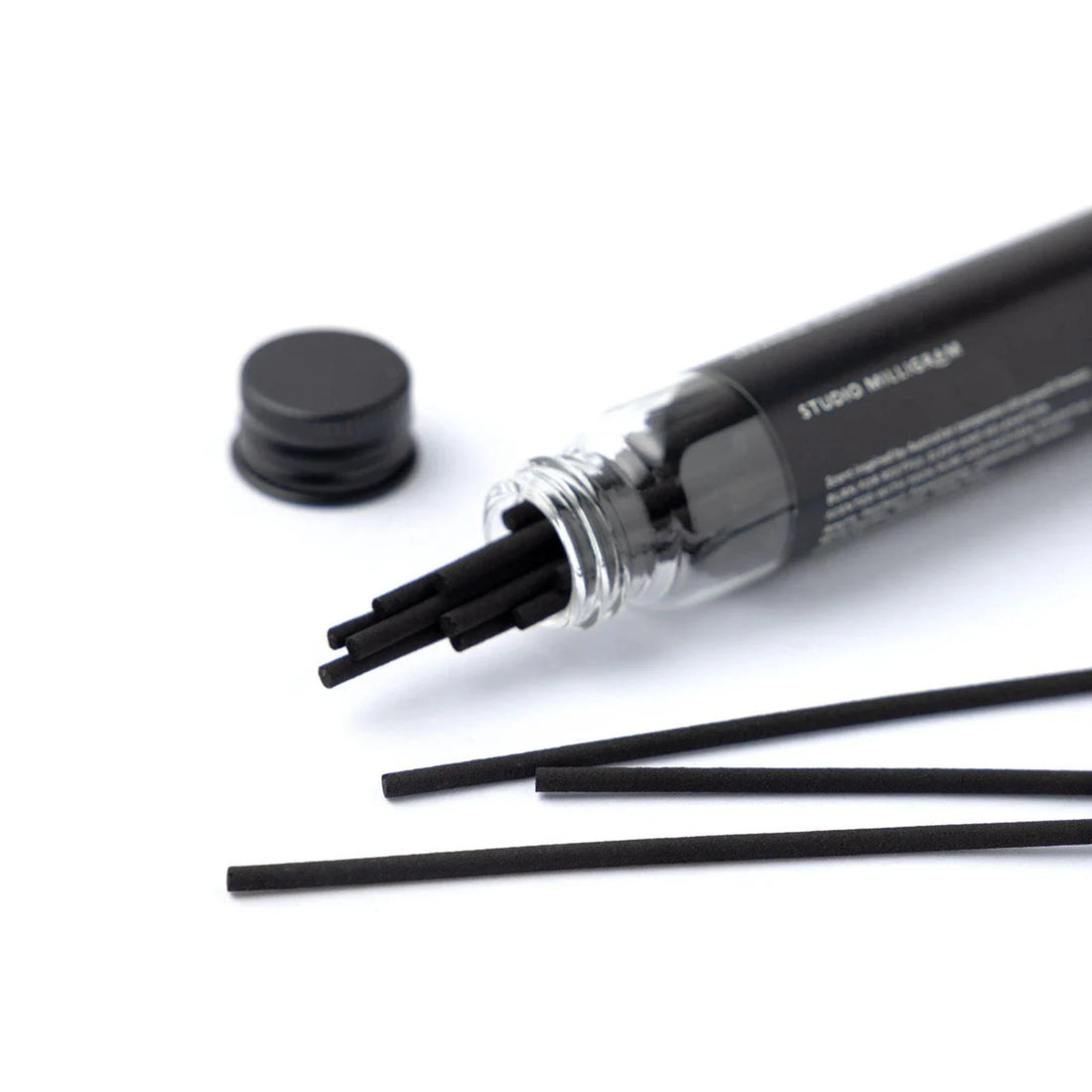 A glass vial of black incense sticks on white surface. 