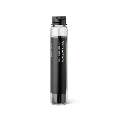 A glass vial of black incense sticks with the Study of Trees fragrance by Studio Milligram.