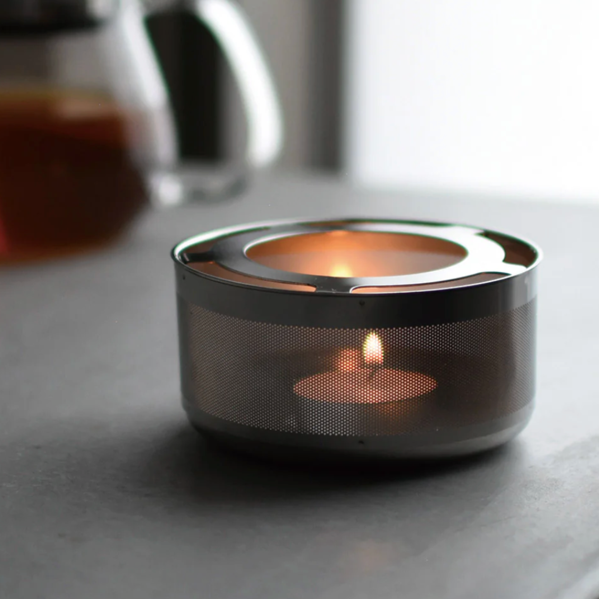 Metallic tea light holder with a lit candle on a gray surface