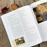 Open book on a wooden surface with pages about fungi, surrounded by autumn leaves.