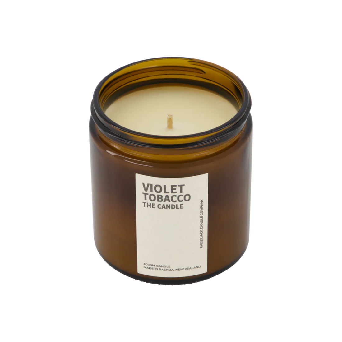 A large amber glass jar with brass lid containing violet tobacco candle on white background. 