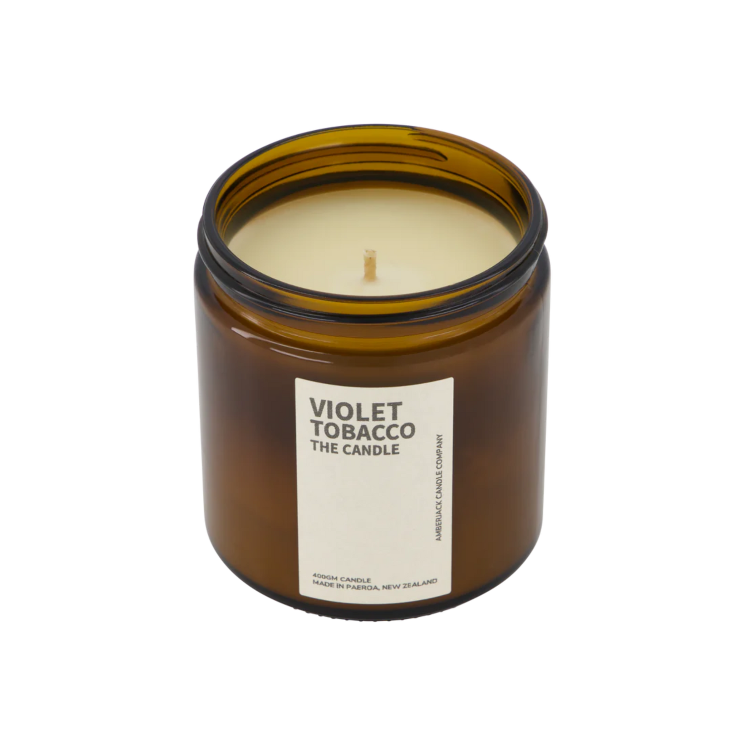 A large amber glass jar with brass lid containing violet tobacco candle on white background. 