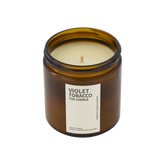 A large amber glass jar with brass lid containing violet tobacco candle on white background. 