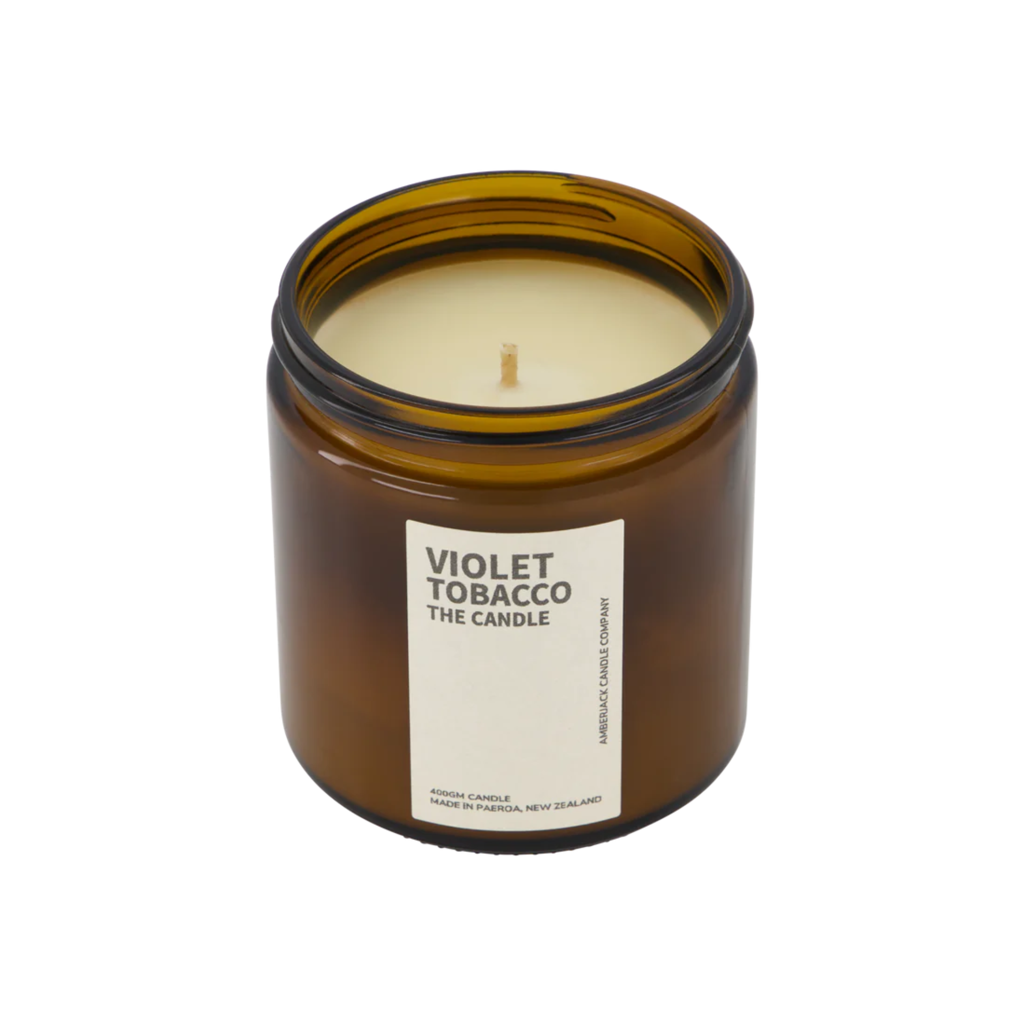 A large amber glass jar with brass lid containing violet tobacco candle on white background. 