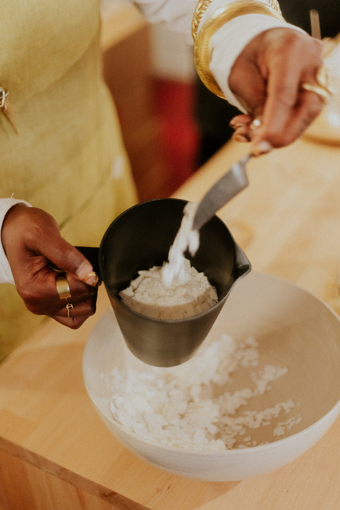 Person pouring flour from a black measuring cup into a white bowl on a wooden surface.